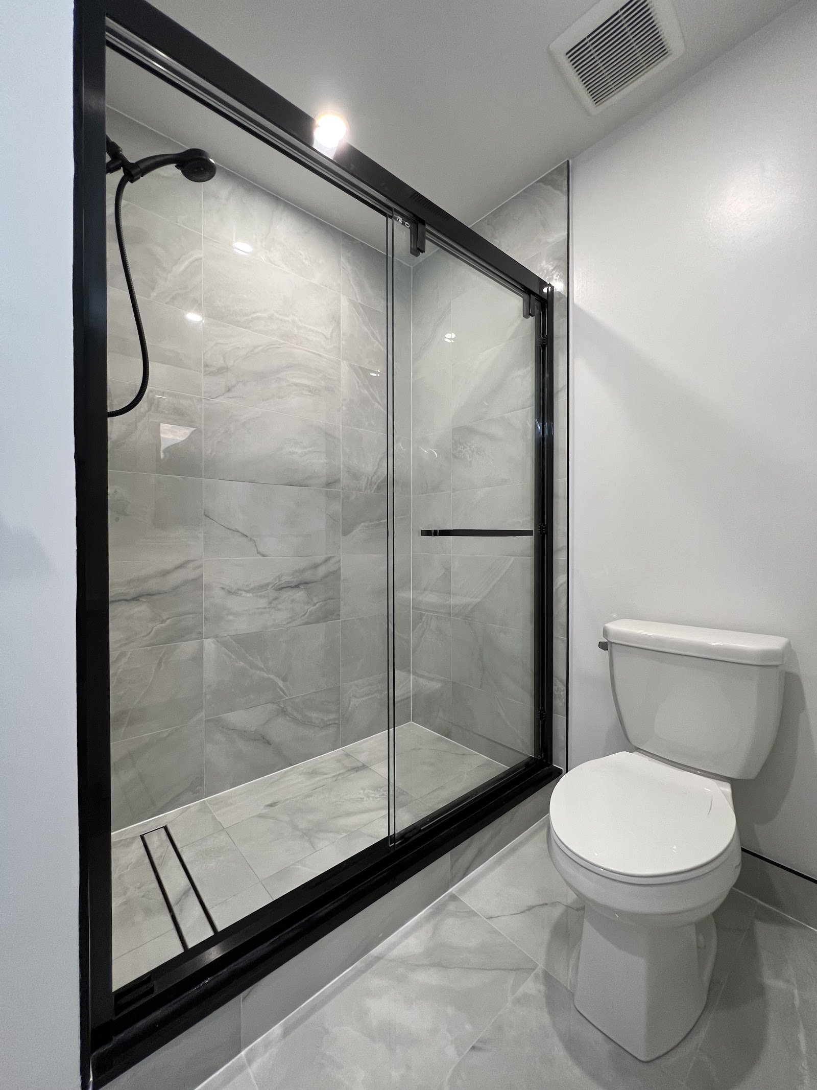 Renovated bathroom with black-framed glass shower and grey marble-look tile