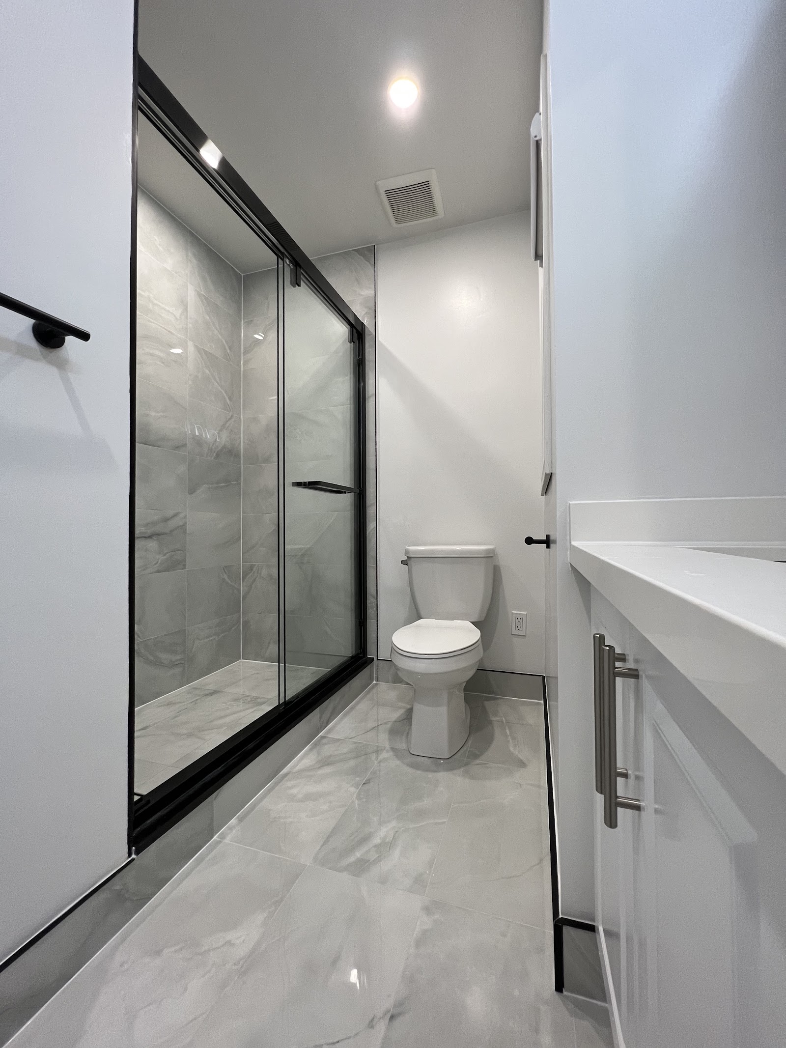 Second angle of renovated bathroom with black-framed shower, new vanity and marble-look floor