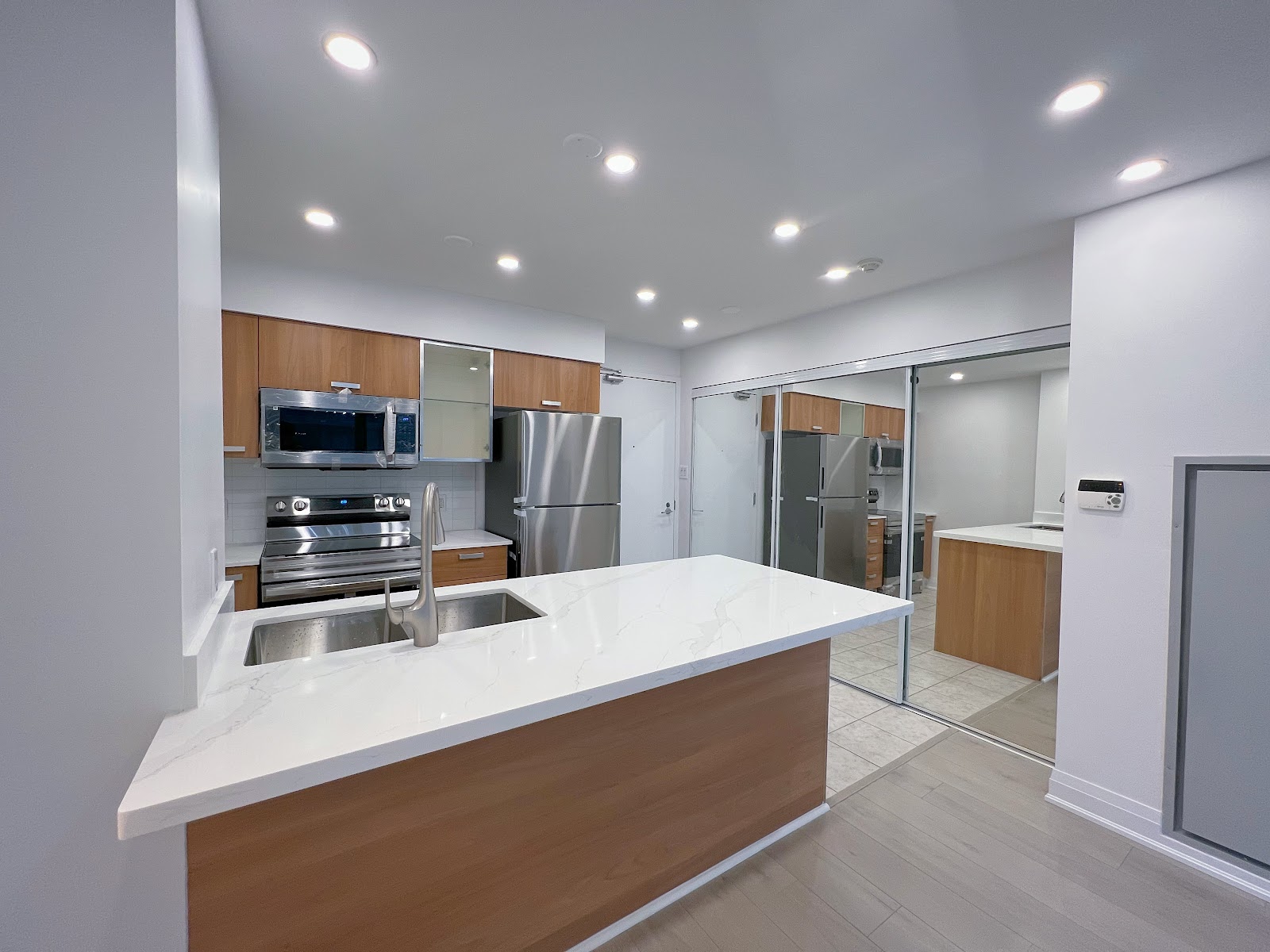 Renovated condo kitchen with quartz island, wood cabinetry and pot lights